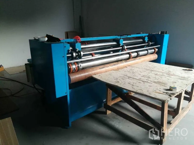 Factory for sale in Bang Len, Nakhon Pathom - Blue roller machine beside a workbench in the manufacturing zone.