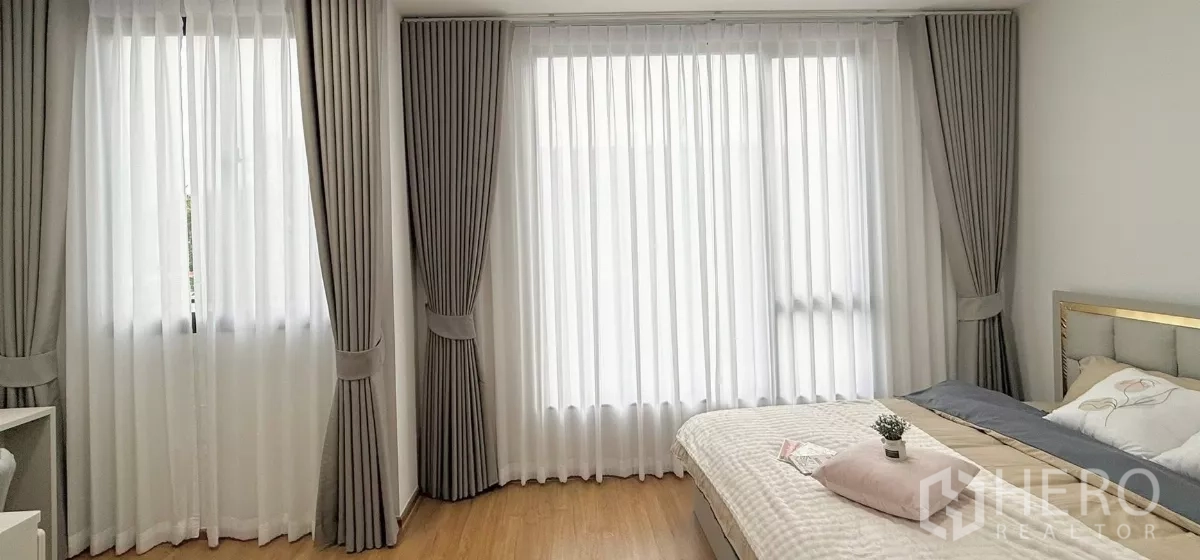 Townhouse for rent in Bang Phli, Samut Prakan - Corner of master bedroom with three tall windows and drapes.