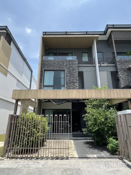 联排别墅 出租在Lat Phrao, Bangkok - 現代三層連排別墅外觀，石材立面、陽台與庭院鐵門，綠植點綴。