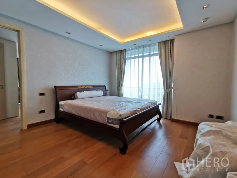 คอนโด ให้เช่าหรือขายในPhaya Thai, Bangkok - ห้องนอนหลัก ฝ้าซ่อนไฟ เตียงไม้ และผ้าม่านโปร่งเปิดสู่วิวระเบียง