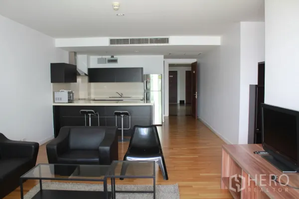 Condominium for rent in Sathon, Bangkok - Open-plan living room with black leather sofas, glass coffee tables, wood floors, and a modern kitchen with island and bar stools.