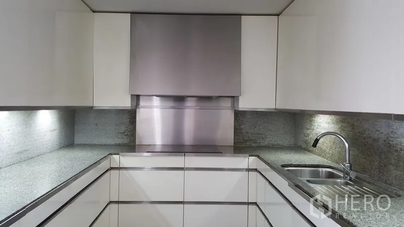 Condominium for rent in Sathon, Bangkok - Modern U-shaped kitchen with white cabinetry, stone countertops, and a stainless-steel backsplash.