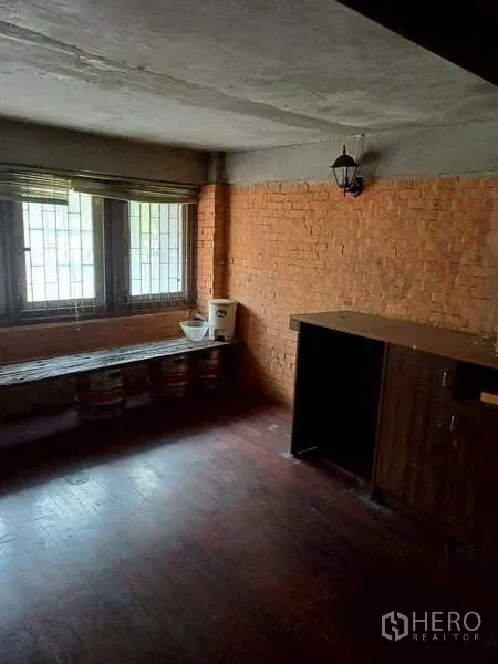 Shophouse for rent in Pom Prap Sattru Phai, Bangkok - Upper-floor room with exposed brick wall, barred windows and dark wooden flooring.