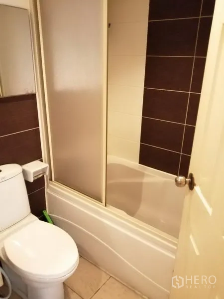 公寓 出租在Watthana, Bangkok - 浴室配浴缸与坐便器，瓷砖墙面与推拉淋浴屏。