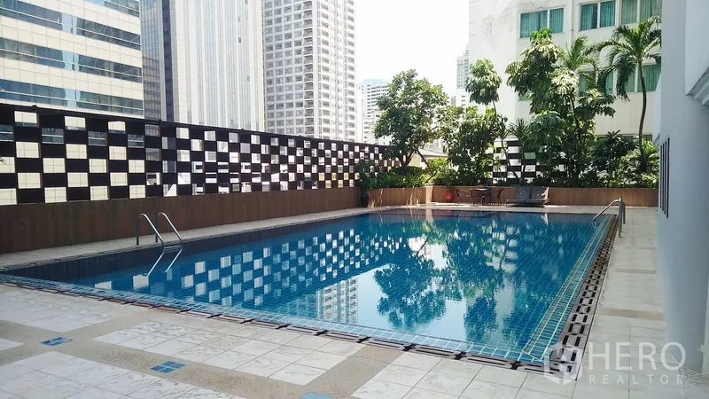 Condominium for sale in Watthana, Bangkok - Outdoor swimming pool deck surrounded by city buildings and greenery.