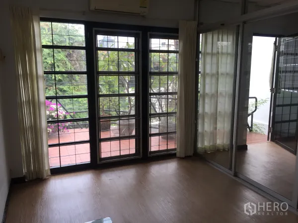 Townhouse for rent in Khlong Toei, Bangkok - Living area with floor-to-ceiling sliding doors opening to a leafy terrace.
