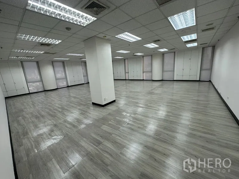 Office Space for rent - Expansive open-plan office with central column, multiple windows, built-in cabinets and grid ceiling lighting.