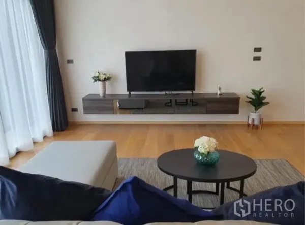 Condominium for rent in Watthana, Bangkok - Living area with sofa, coffee table, floating TV console, and large curtained windows.