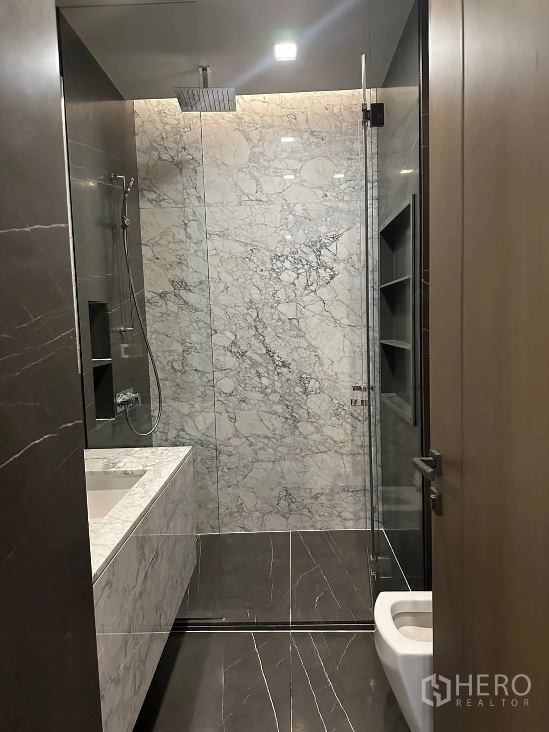 Condominium for rent or sale in Watthana, Bangkok - Rain shower and glass enclosure in a stone-finish bathroom.