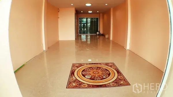 Shophouse for sale in Lam Luk Ka, Pathum Thani - Open-plan ground floor of the shophouse with glossy tiles, decorative medallion and glass door to the rear.
