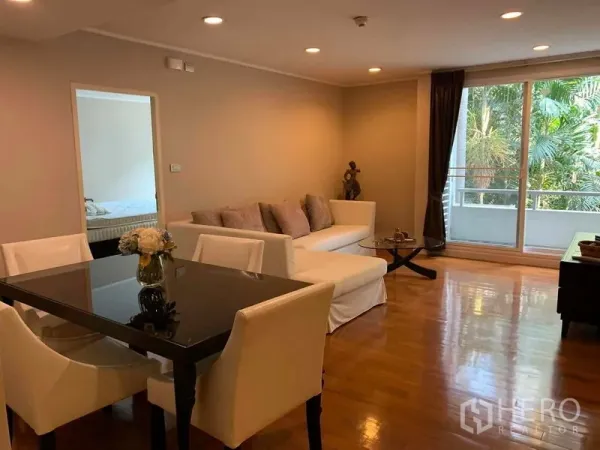 Condominium for rent in Pathum Wan, Bangkok - Dining table and white sofa in a living area opening to a balcony with lush views.