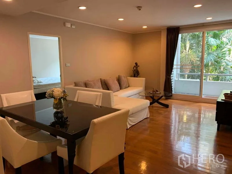 Condominium for rent in Pathum Wan, Bangkok - Dining table and white sofa in a living area opening to a balcony with lush views.