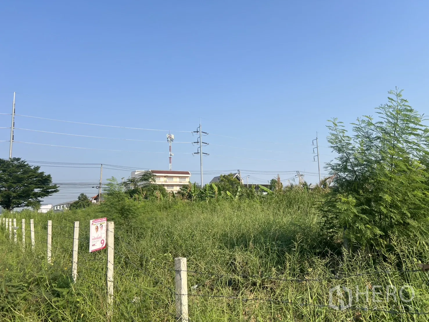 Land for sale in Lat Krabang, Bangkok - Fenced plot with utility poles and a low-rise building in the background.