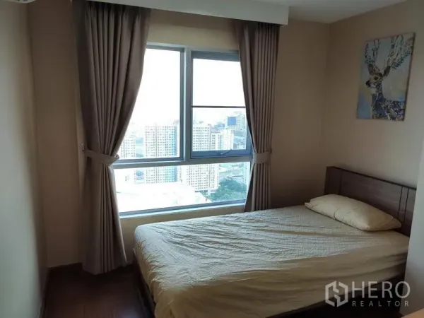 Condominium for rent in Huai Khwang, Bangkok - Bedroom with large window and city skyline view, blackout curtains and neutral decor.