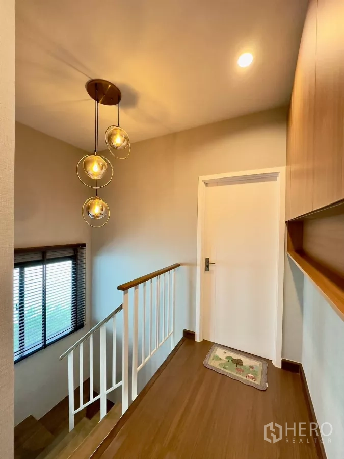 独立式住宅 出租在Samut Prakan - 楼梯平台配现代吊灯、采光窗与木地板。