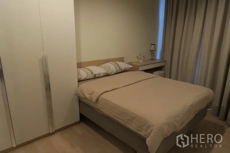 Condominium for rent in Huai Khwang, Bangkok - Second bedroom with double bed, built‑in wardrobe, bedside table and blackout curtains.