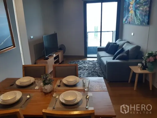 Condominium for rent in Khlong Toei, Bangkok - Bright living and dining area with gray sofa, TV unit and balcony in a Sukhumvit condo.