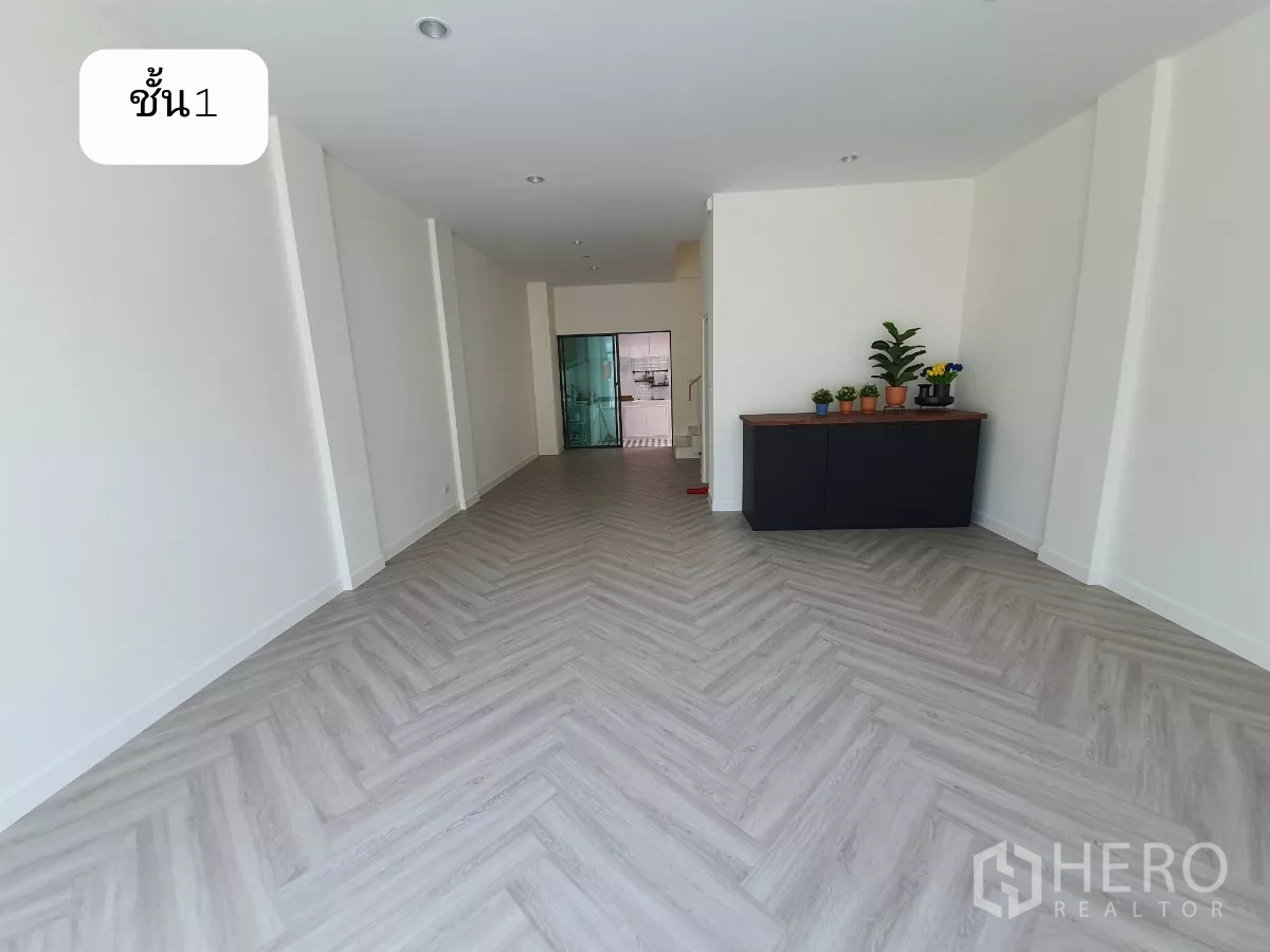 Home Office for rent or sale in Prawet, Bangkok - Open-plan ground floor of the home office with herringbone flooring, white walls, a side cabinet with plants and a rear glass partition.