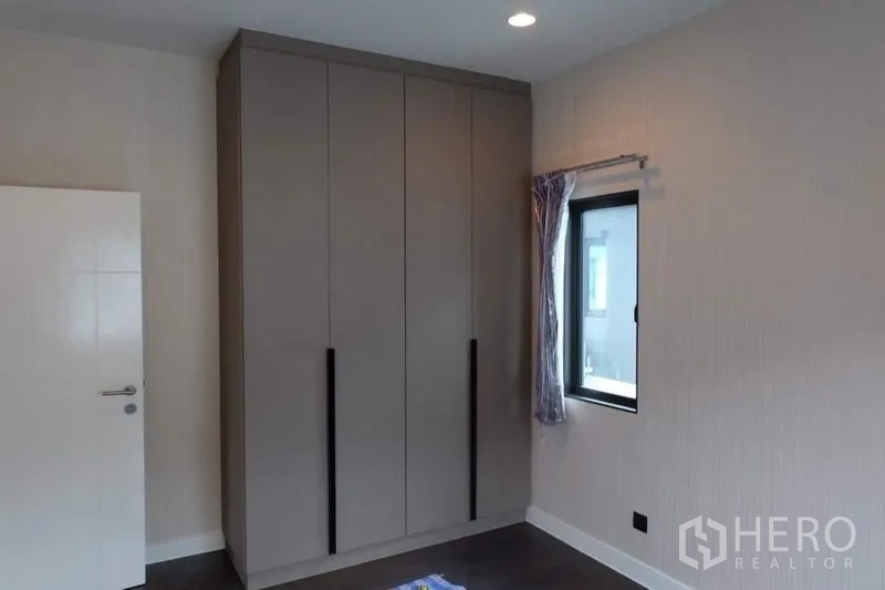 Detached House for rent in Bang Kapi, Bangkok - Bedroom fitted with a tall matte wardrobe, recessed lighting and a small side window.