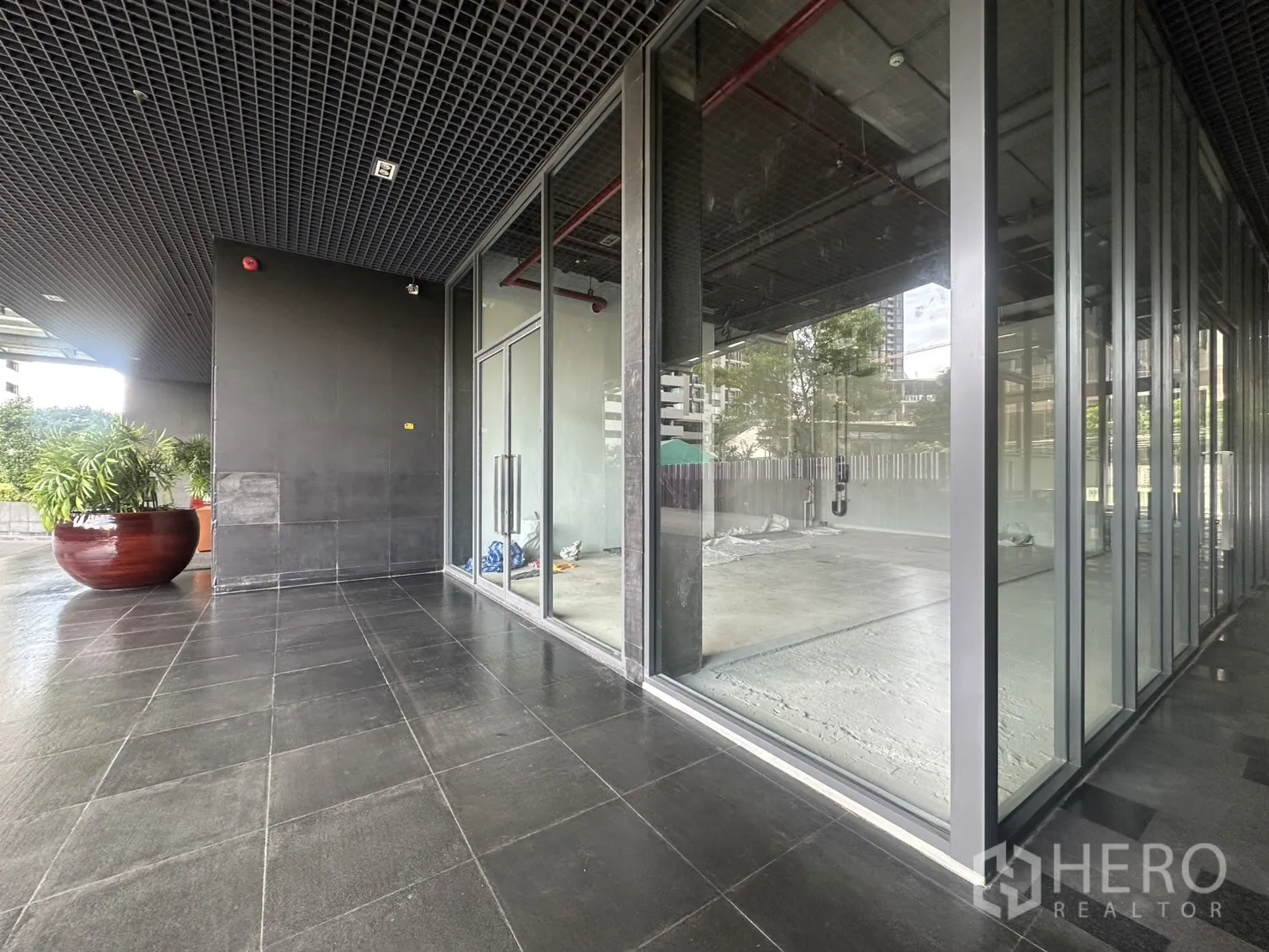 Retail Space for rent in Khlong Toei, Bangkok - Covered outdoor walkway and corner glass storefront with planters and tiled terrace.