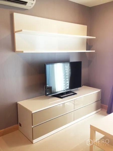 Condominium for rent or sale in Mueang Samut Prakan, Samut Prakan - Media wall with flat-screen TV, glossy cabinet, floating shelf and wall AC.