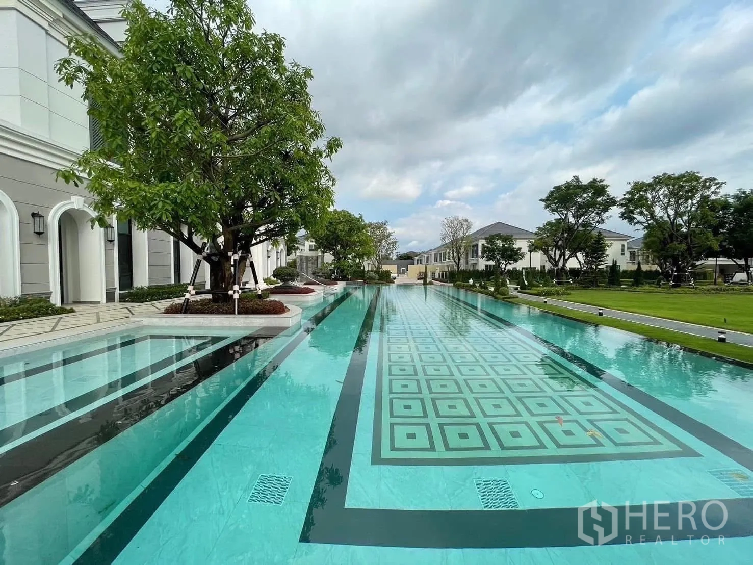 独立式住宅 出租在Bang Phli, Samut Prakan - 长条泳道与几何拼花池底，周围绿树草地。