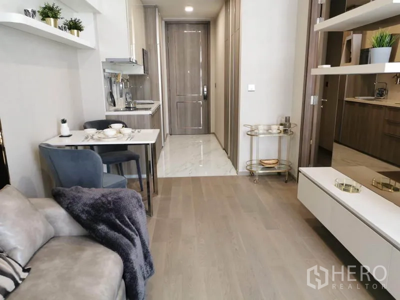 Condominium for rent in Watthana, Bangkok - Bright living room with sofa, dining table, built-in shelves, and corridor leading to the bedroom and entry.