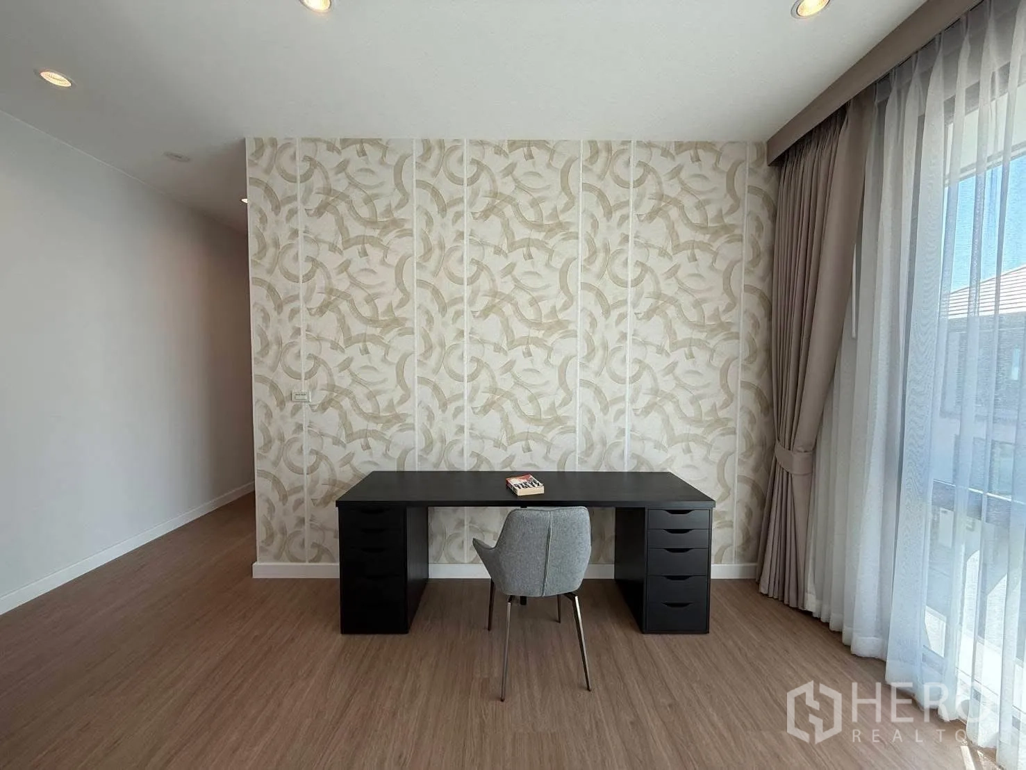 Detached House for rent in Bang Phli, Samut Prakan - Work corner featuring a black desk, grey chair, and decorative patterned wallpaper beside tall windows.