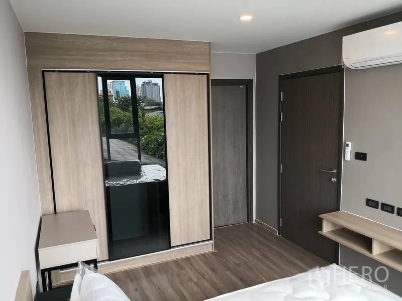 Condominium for rent or sale in Watthana, Bangkok - Bedroom with floor-to-ceiling wardrobe, air conditioner, and window showing city and green views.
