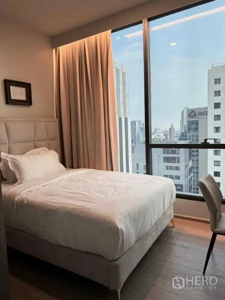 Condominium for rent in Watthana, Bangkok - Secondary bedroom with upholstered headboard, work desk, and tall window city outlook.