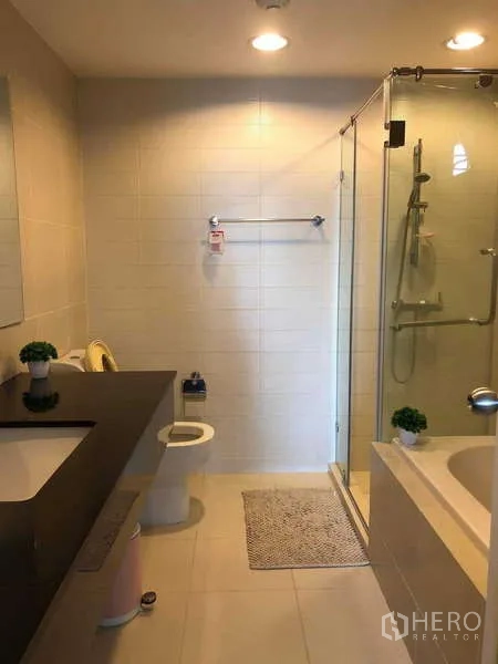 Condominium for sale in Huai Khwang, Bangkok - Modern bathroom with glass-enclosed shower, bathtub, vanity and tiled walls.