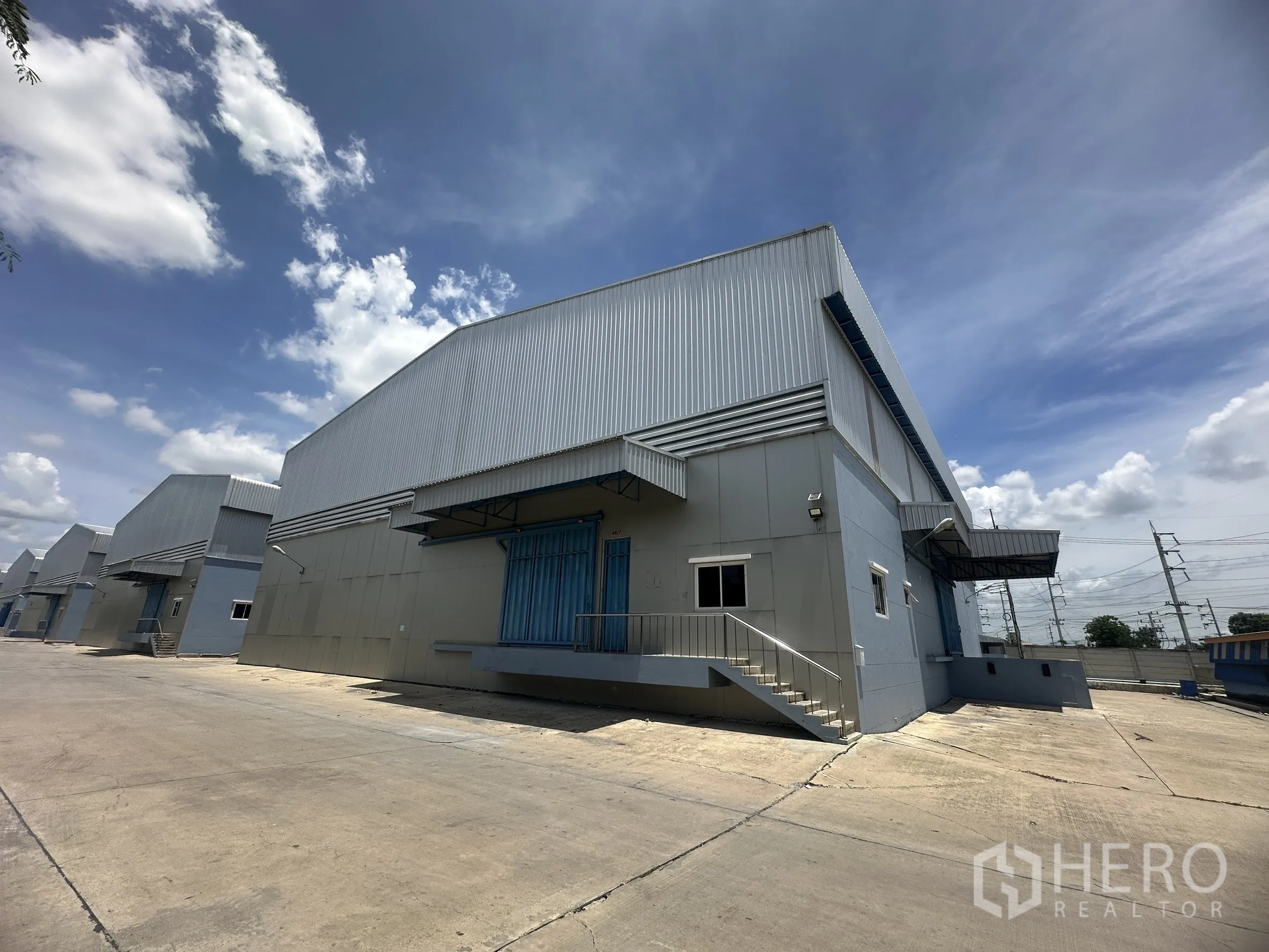 Warehouse for rent in Lat Lum Kaeo, Pathum Thani - Row of industrial warehouses with canopies and dock-high loading bays along a wide driveway.