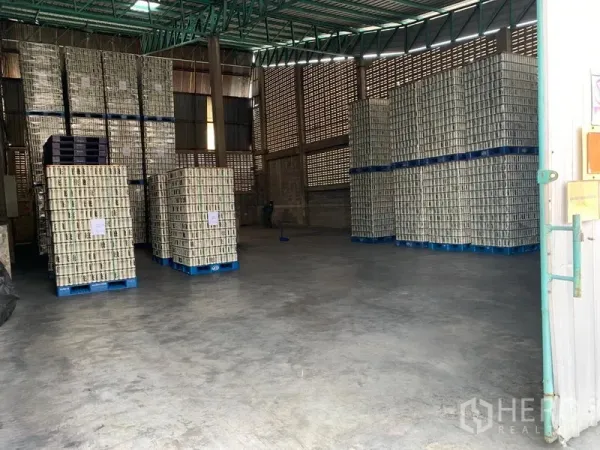 货栈 出租在Mueang Pathum Thani, Pathum Thani - 仓库内部，高挑层高，通风砖墙，整齐堆放的托盘，混凝土地面。