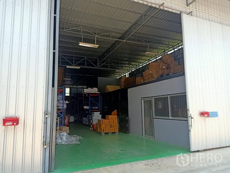 คลังสินค้า ให้เช่าในBang Kapi, Bangkok - ประตูบานสไลด์เปิดกว้าง เผยให้เห็นโกดังเพดานสูง โครงเหล็ก พื้นอีพ็อกซีสีเขียว และชั้นวางสินค้า