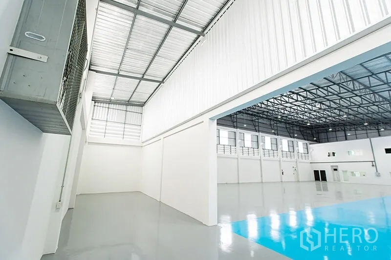 Warehouse for rent in Bang Bo, Samut Prakan - Side aisle and mezzanine-ready zone beneath a high sheet-metal roof with skylights.