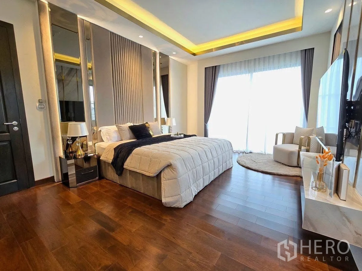 Detached House for rent or sale in Bang Phli, Samut Prakan - Spacious master bedroom with king bed, cove lighting, wood floors and seating by full-height windows.