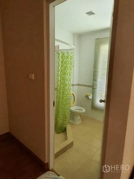 Townhouse for rent in Bueng Kum, Bangkok - Bright bathroom with a corner shower and green curtain, toilet, and a window with blinds.