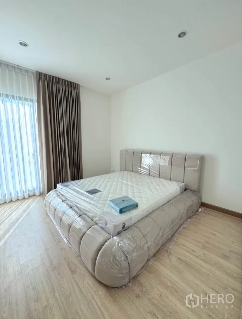 Detached House for rent in Samut Prakan - Master bedroom with upholstered bed, wood floor and sheer curtains.