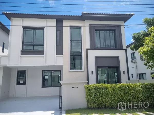 Detached House for rent in Bang Phli, Samut Prakan - Modern two-storey detached house facade with large windows, hedge and a covered driveway in Bang Phli.