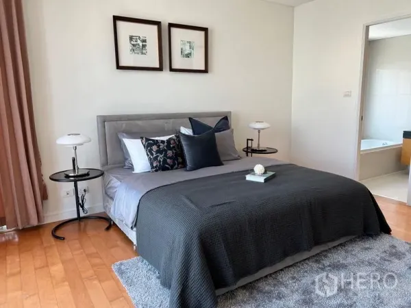 公寓 出租在Watthana, Bangkok - 主卧配软包床、床头灯与木地板，可见套内卫浴。