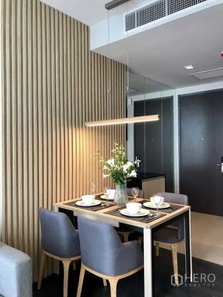 Condominium for rent in Watthana, Bangkok - Compact dining nook for four with grey chairs and a linear pendant beside a wood slat feature wall.
