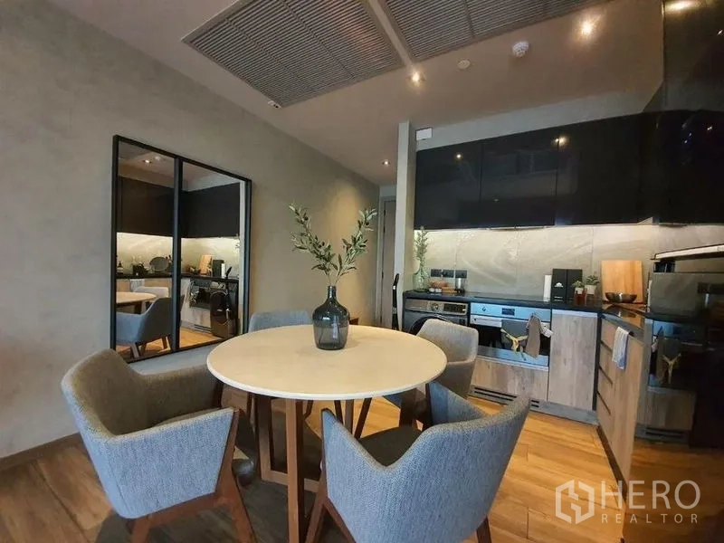 Condominium for rent or sale in Watthana, Bangkok - Dining nook with round table and four upholstered chairs beside the fitted kitchen.