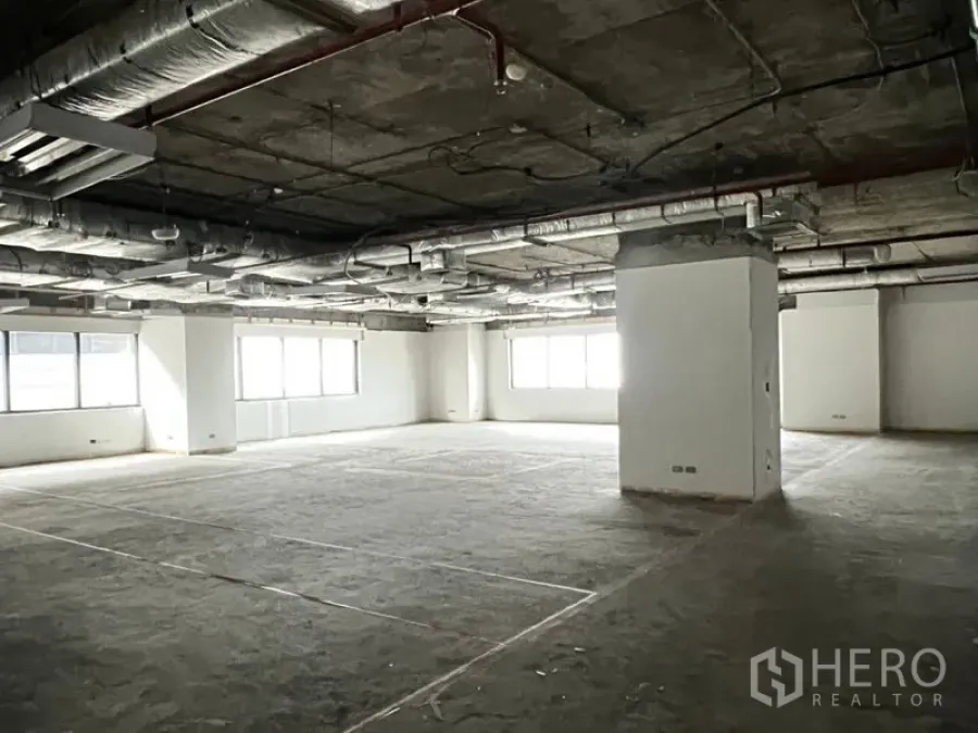 Office Space for rent - Large bare-shell office floor with exposed ceiling ductwork, columns, and wide windows providing natural light.