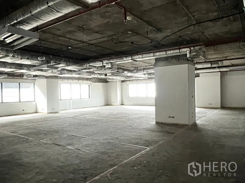 Office Space for rent - Large bare-shell office floor with exposed ceiling ductwork, columns, and wide windows providing natural light.