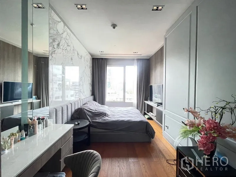 Condominium for rent in Pathum Wan, Bangkok - Primary bedroom with large window, marble accent wall, vanity and wood flooring.