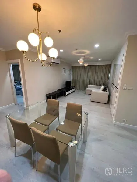 Condominium for sale in Sathon, Bangkok - Living room view with sectional sofa and TV console, glass dining table under chandelier.