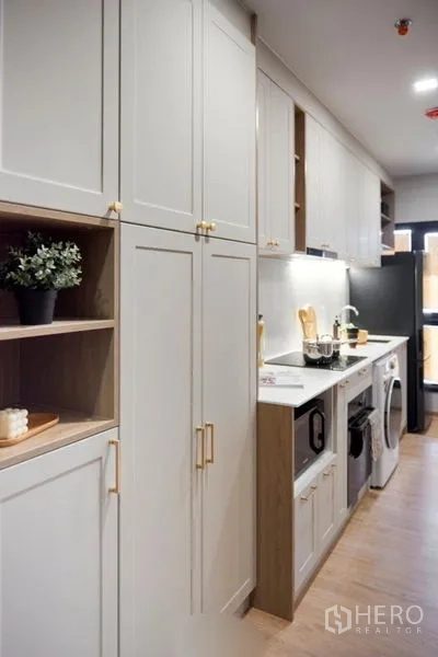 Condominium for sale in Suan Luang, Bangkok - Modern galley kitchen with white shaker cabinets, gold handles, built-in appliances and under-cabinet lighting.