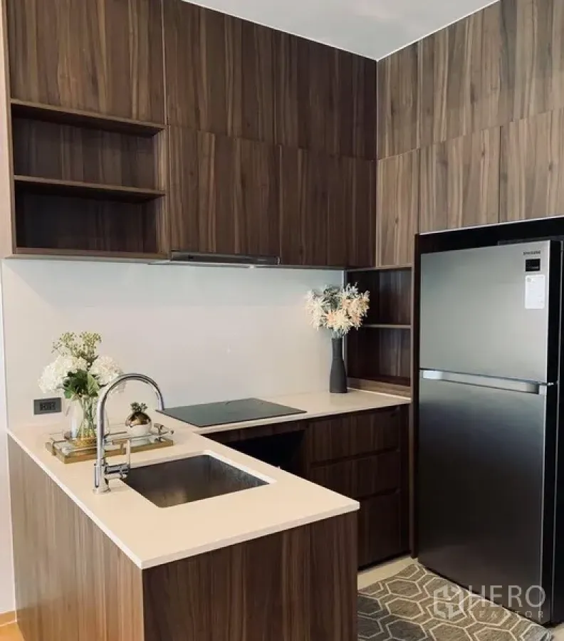 Condominium for rent in Watthana, Bangkok - Modern L-shaped kitchen with wood cabinetry, quartz countertop, sink, cooktop and refrigerator.
