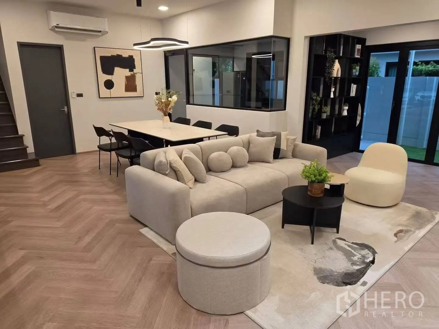ทาวน์เฮาส์ for rent in Bang Phli, Samut Prakan - ห้องนั่งเล่นอบอุ่นมีโซฟา ออตโตมัน โต๊ะทานอาหาร งานศิลป์ และประตูกระจกออกสู่สวน