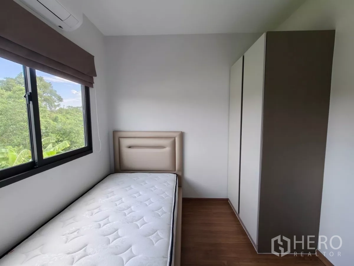 Townhouse for rent in Bang Phli, Samut Prakan - Cozy second bedroom with single bed, wardrobe and window overlooking green trees.